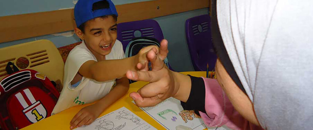 Ali håller sin speciallärare i handen. Framför dem finns några teckningar.