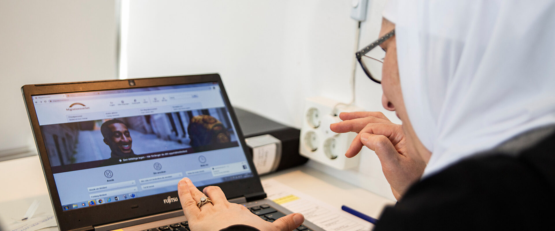 Kvinna i slöja och glasögon arbetar på dator.