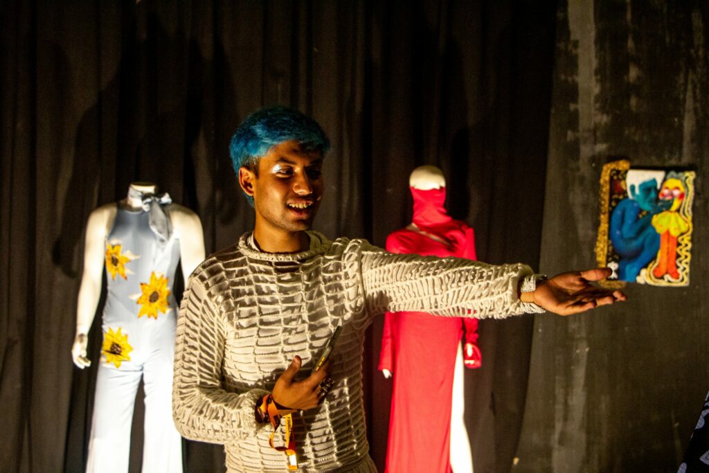 Konstnär framför designkläder. Håller i en tavla.