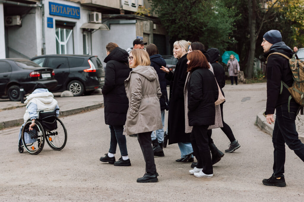 En rullstolsburen kvinna visar vägen över vägen för en en liten klunga människor.